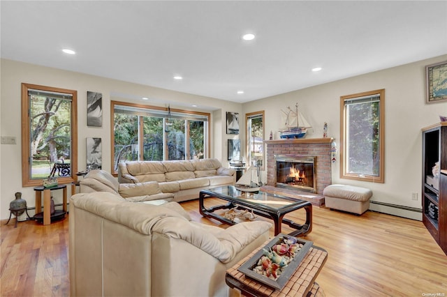 living room featuring baseboard heating, light hardwood / wood-style flooring, a healthy amount of sunlight, and a brick fireplace