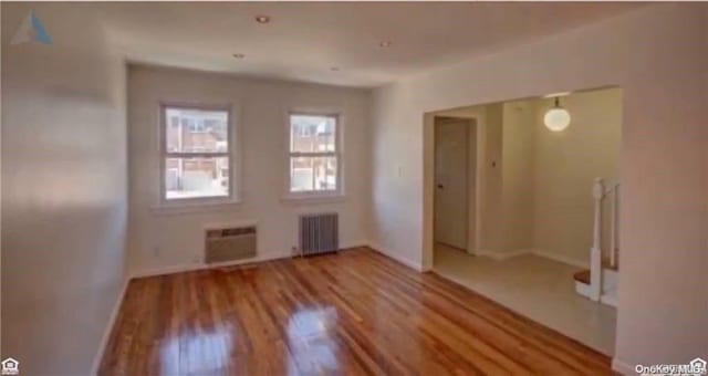 spare room featuring a wall mounted air conditioner, light hardwood / wood-style floors, and radiator heating unit