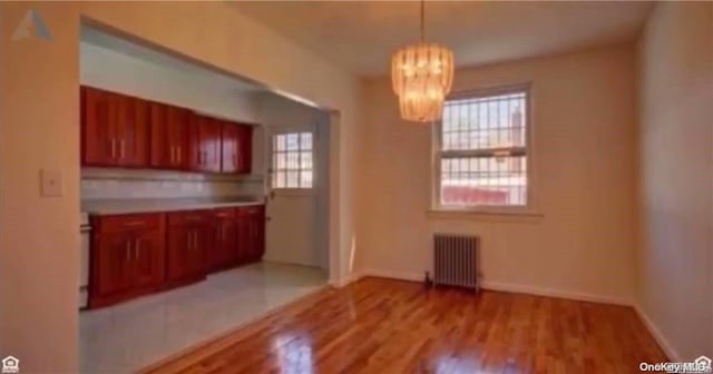 kitchen with a chandelier, light hardwood / wood-style floors, radiator, and a healthy amount of sunlight