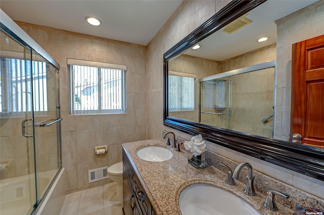 full bathroom with vanity, bath / shower combo with glass door, tile patterned flooring, toilet, and tile walls