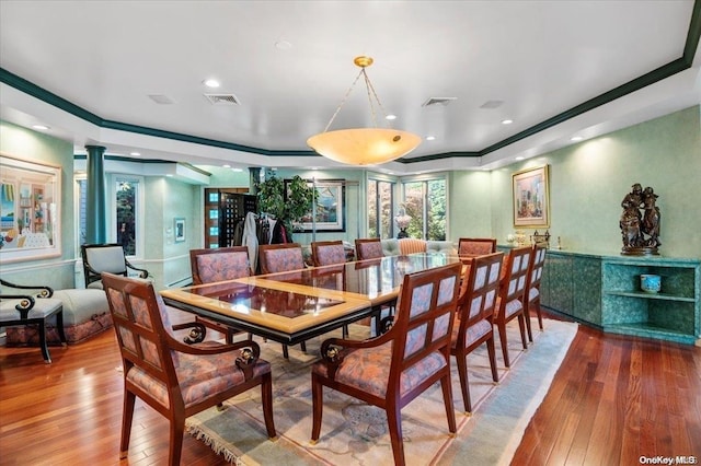 dining space featuring a raised ceiling, wood-type flooring, and decorative columns