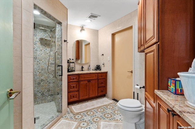 bathroom with tile patterned floors, vanity, tile walls, toilet, and a shower with shower door