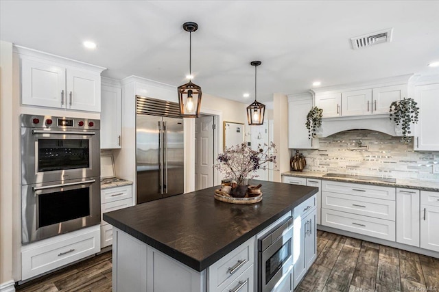 kitchen with backsplash, pendant lighting, built in appliances, white cabinets, and a center island