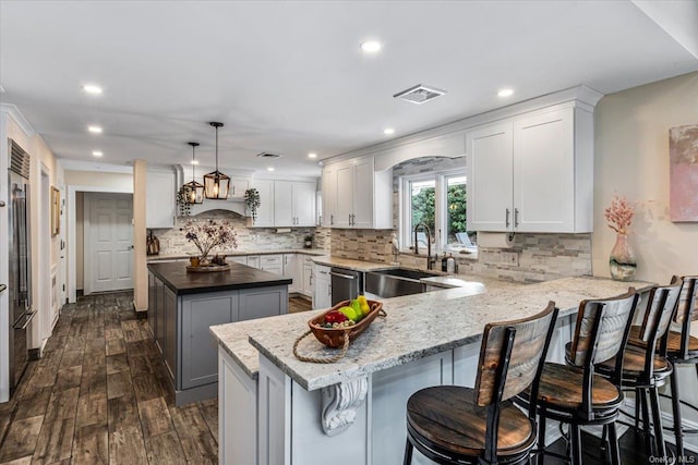 kitchen with stainless steel dishwasher, a kitchen island, sink, pendant lighting, and white cabinetry