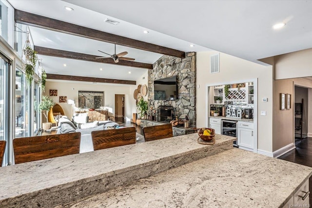 kitchen with beam ceiling, wine cooler, light stone counters, and a fireplace