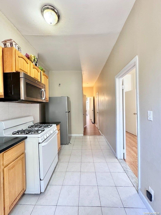 kitchen featuring light wood-type flooring, light brown cabinetry, fridge, and gas range gas stove