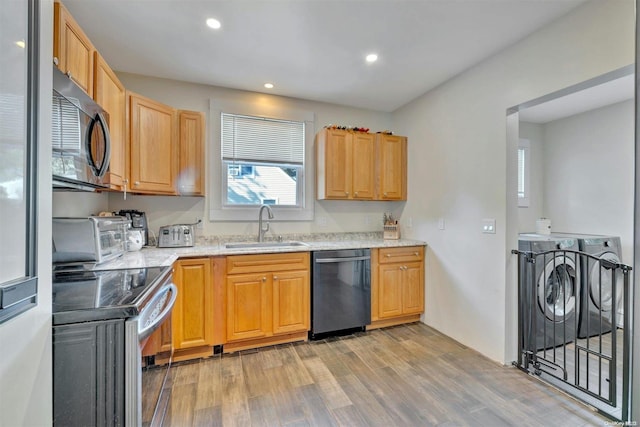 kitchen with light stone countertops, stainless steel appliances, sink, washing machine and dryer, and light hardwood / wood-style floors