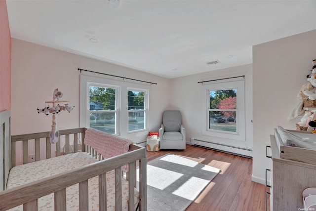 bedroom featuring a crib, light hardwood / wood-style flooring, and a baseboard radiator