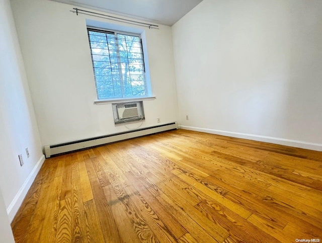 spare room featuring a wall mounted air conditioner, light wood-type flooring, and a baseboard heating unit