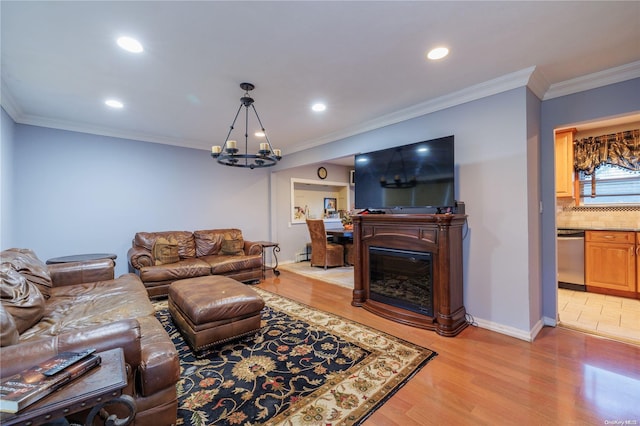 living room with a notable chandelier, crown molding, a glass covered fireplace, light wood-type flooring, and baseboards