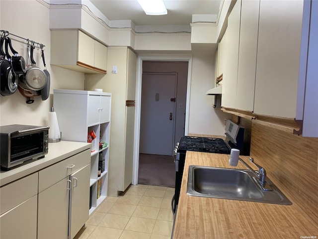 kitchen featuring light tile patterned flooring, sink, and stainless steel range with gas stovetop