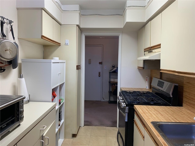 kitchen featuring white cabinetry, light tile patterned floors, sink, and stainless steel range with gas stovetop