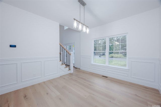 unfurnished living room with light hardwood / wood-style floors, vaulted ceiling, and an inviting chandelier