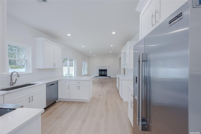 kitchen with sink, stainless steel appliances, kitchen peninsula, light hardwood / wood-style floors, and white cabinets