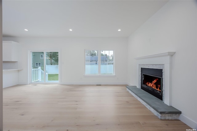 unfurnished living room with a high end fireplace, a healthy amount of sunlight, and light hardwood / wood-style floors