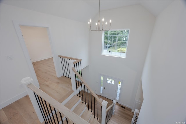 stairs with hardwood / wood-style floors, an inviting chandelier, and vaulted ceiling