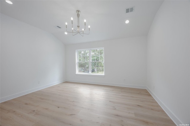 spare room with a chandelier, light wood-type flooring, and lofted ceiling