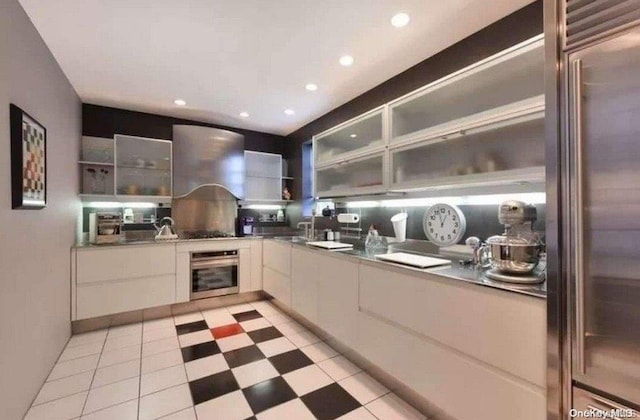 kitchen featuring white cabinets, wall chimney range hood, sink, and appliances with stainless steel finishes