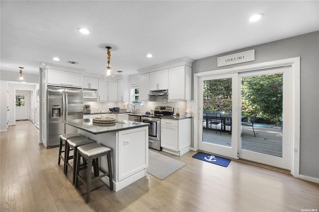 kitchen with a kitchen bar, appliances with stainless steel finishes, light hardwood / wood-style floors, white cabinetry, and hanging light fixtures