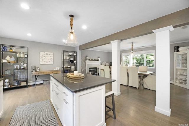 18 Diane Dr, Manorville, NY 11949 - kitchen with decorative columns, dark countertops, wood finished floors, a kitchen island, and white cabinets