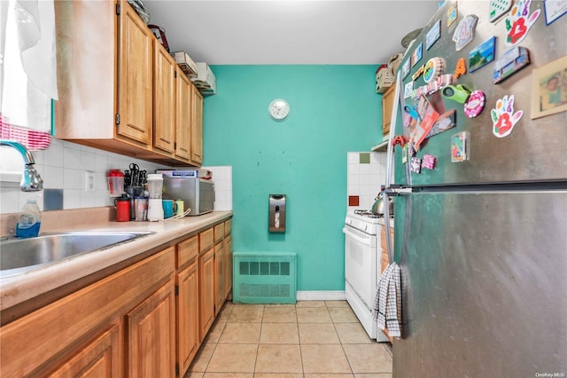 kitchen with stainless steel refrigerator, white gas range, sink, tasteful backsplash, and light tile patterned floors