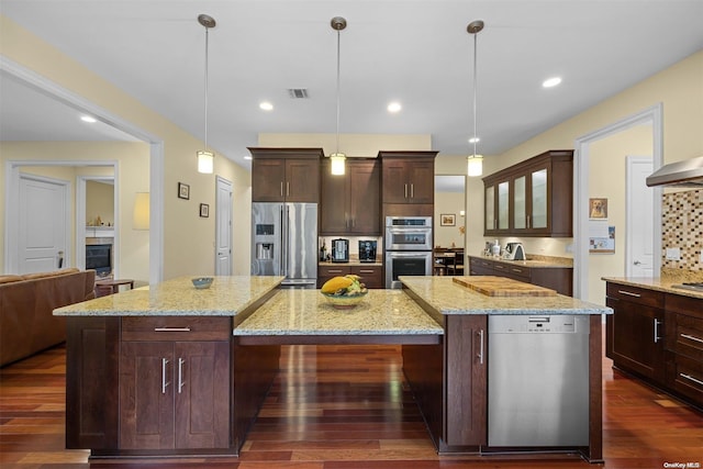 kitchen featuring dark wood-type flooring, decorative light fixtures, a kitchen island, stainless steel appliances, and light stone countertops