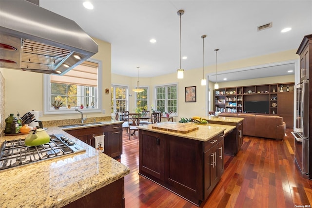 kitchen featuring pendant lighting, appliances with stainless steel finishes, light stone countertops, a kitchen island, and exhaust hood