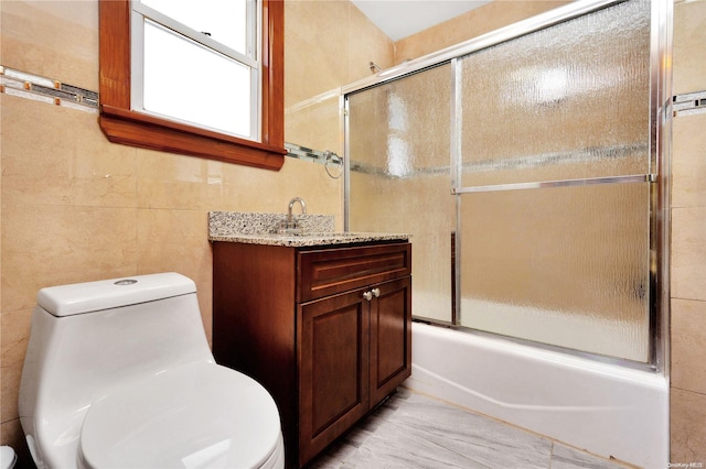 full bathroom featuring toilet, vanity, tile walls, and combined bath / shower with glass door