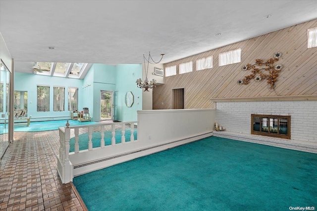 interior space featuring baseboard heating, lofted ceiling with skylight, wood walls, and a brick fireplace