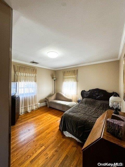 bedroom featuring multiple windows, hardwood / wood-style floors, a textured ceiling, and ornamental molding