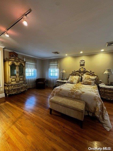 bedroom with ornamental molding, rail lighting, and dark wood-type flooring