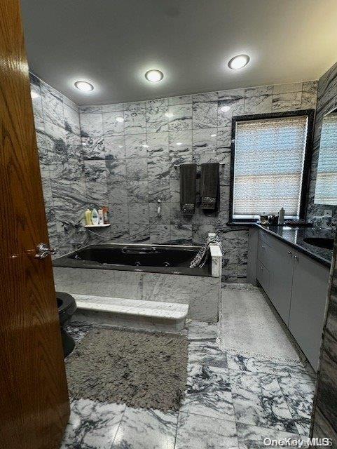 bathroom with vanity, tile walls, and a tub