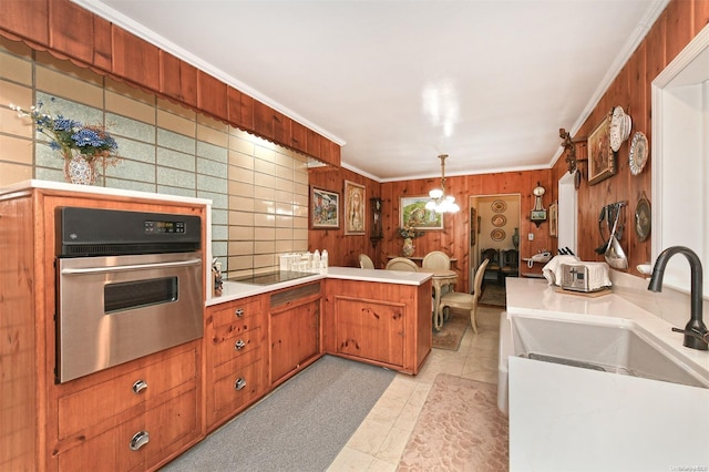 kitchen with kitchen peninsula, pendant lighting, ornamental molding, and stainless steel oven