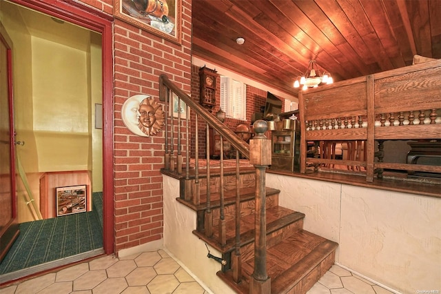 stairs featuring tile patterned floors, wooden ceiling, a chandelier, and brick wall