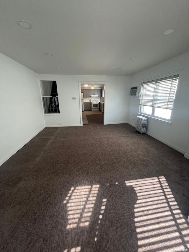 unfurnished living room with radiator heating unit, dark carpet, and a wall unit AC