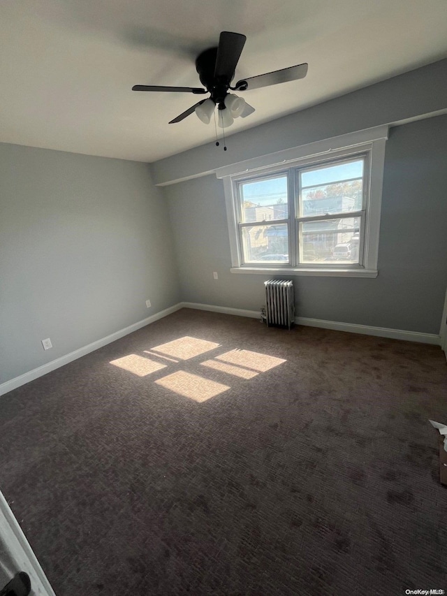 empty room with dark colored carpet, ceiling fan, and radiator heating unit