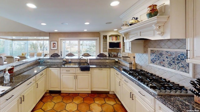 kitchen featuring sink, backsplash, dark stone countertops, kitchen peninsula, and stainless steel gas stovetop