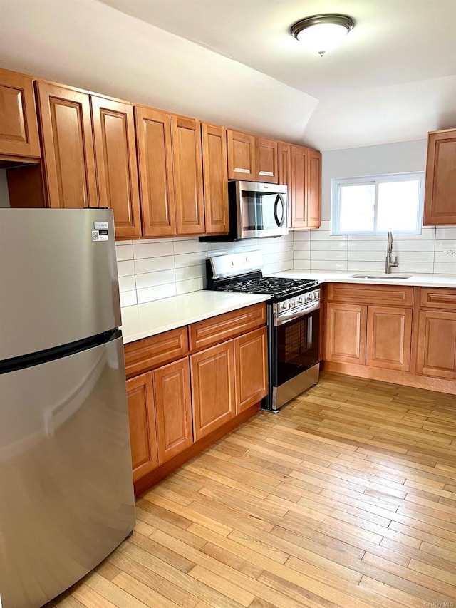 kitchen featuring lofted ceiling, sink, appliances with stainless steel finishes, tasteful backsplash, and light hardwood / wood-style floors