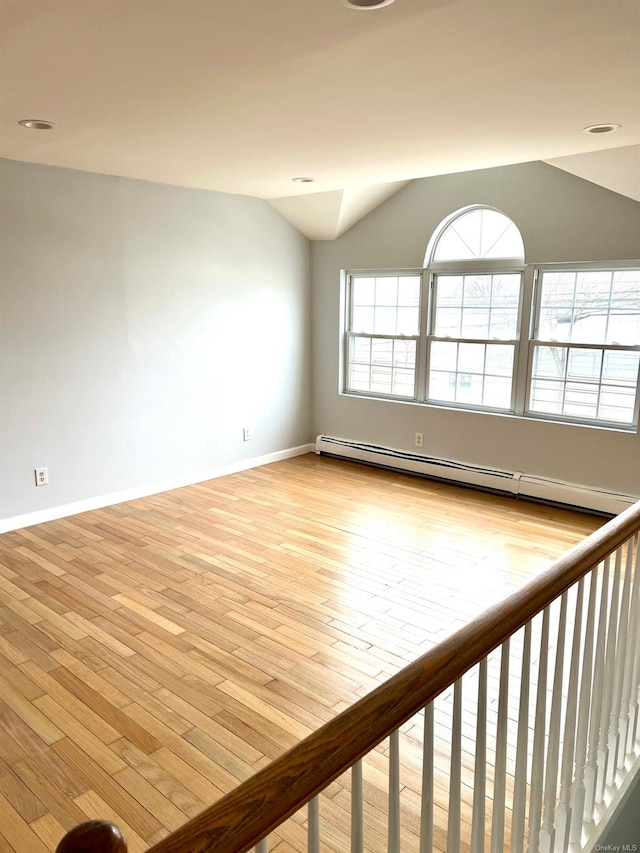 unfurnished room featuring lofted ceiling, baseboard heating, and light hardwood / wood-style flooring