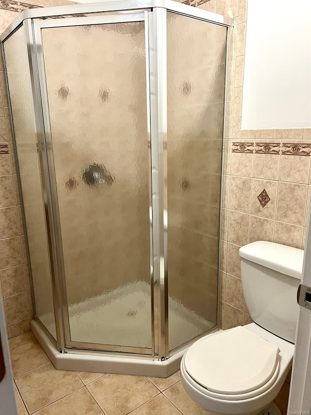 bathroom with tile patterned flooring, tile walls, an enclosed shower, and toilet