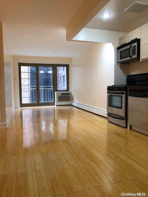 kitchen featuring a wall mounted air conditioner, appliances with stainless steel finishes, light hardwood / wood-style flooring, and baseboard heating