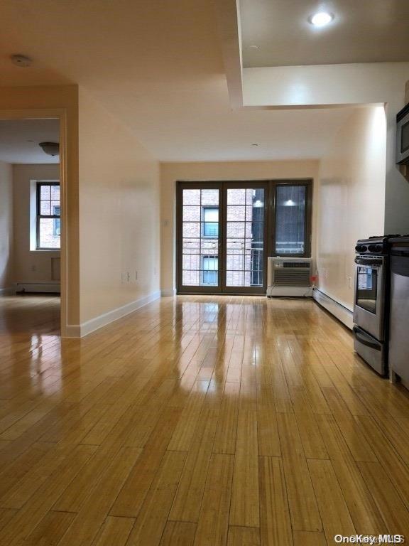 unfurnished living room with a wall mounted AC, light hardwood / wood-style flooring, and baseboard heating