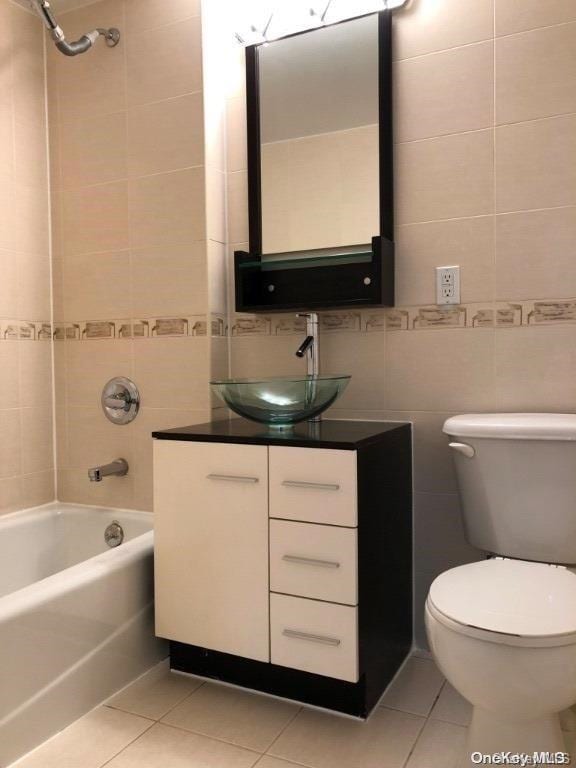 full bathroom with tiled shower / bath combo, tile patterned flooring, toilet, vanity, and tile walls