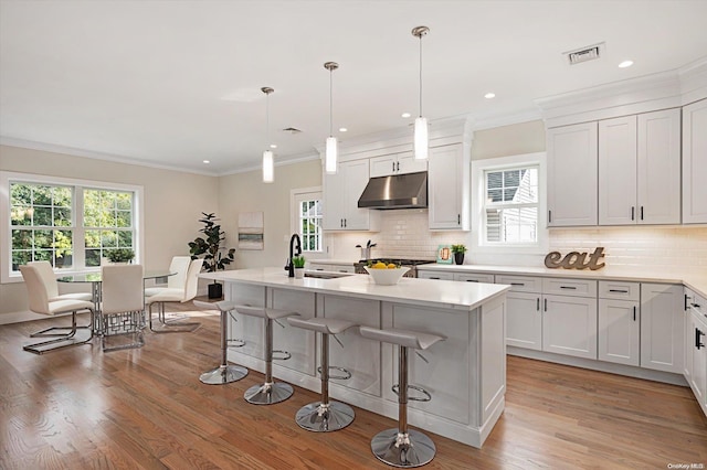 kitchen with sink, decorative light fixtures, a center island with sink, white cabinets, and light wood-type flooring