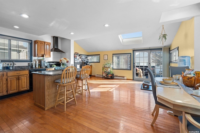 kitchen featuring a wealth of natural light, vaulted ceiling with skylight, wall chimney exhaust hood, and light hardwood / wood-style flooring