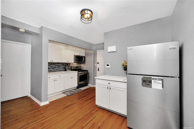 kitchen with light wood-type flooring, backsplash, stainless steel appliances, sink, and white cabinetry