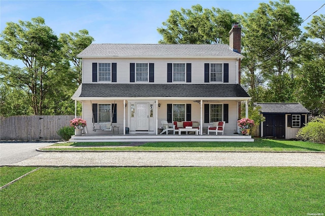 colonial-style house with a storage unit, a porch, and a front yard