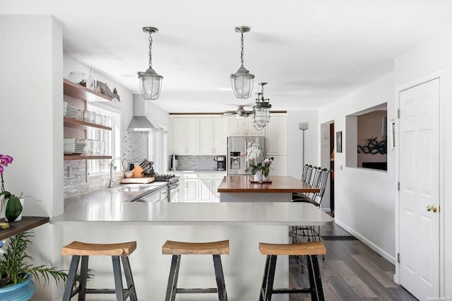 kitchen with a kitchen breakfast bar, wall chimney range hood, hanging light fixtures, dark hardwood / wood-style floors, and appliances with stainless steel finishes