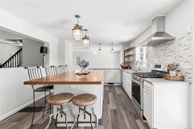 kitchen featuring dark hardwood / wood-style flooring, gas stove, wall chimney range hood, decorative light fixtures, and white cabinets