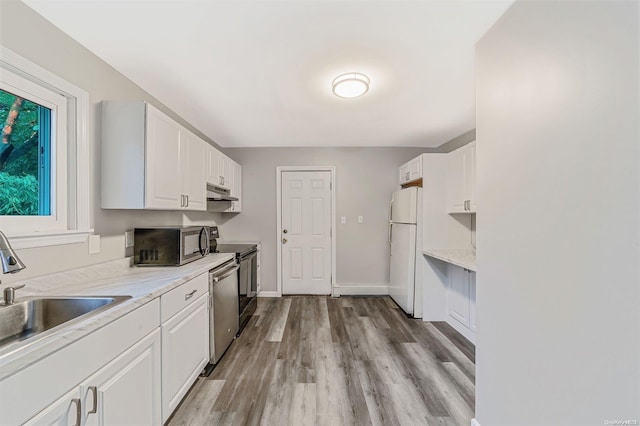 kitchen featuring light wood-type flooring, light stone counters, stainless steel appliances, sink, and white cabinets